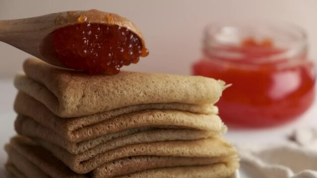 Pancakes or blini with red caviar. Hands pick red caviar in a spoon. Pancakes for Shrovetide.