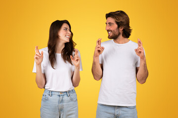 Optimistic young couple in white t-shirts crossing their fingers for good luck