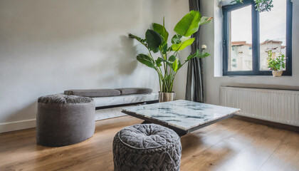 A marble coffee table, poufs, and a houseplant near by the window in a modern white living room.