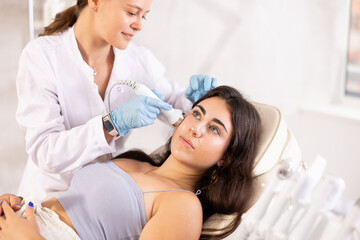 Young brunette girl having facial beauty massage with vibration attachement of beauty machine...