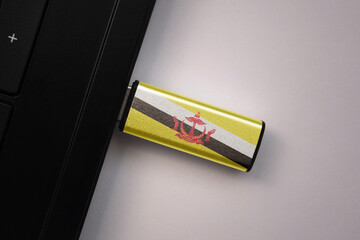usb flash drive in notebook computer with the national flag of brunei on gray background.