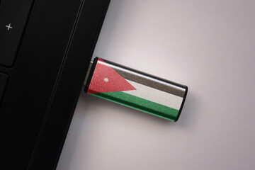 usb flash drive in notebook computer with the national flag of jordan on gray background.