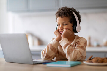 Boring Content. Upset little black boy in headphones looking at laptop screen