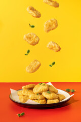 Delicious golden chicken nuggets levitate over a plate on a red and yellow background. Fast food, menu