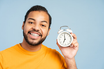 Happy man with dental braces holding alarm clock and smiling isolated