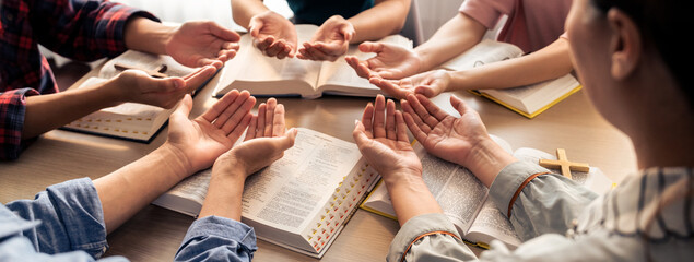 Cropped image of diversity people hand praying together at wooden church on bible book. Group of...
