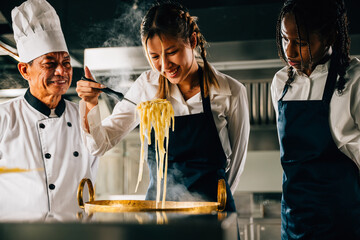 Chef educates in kitchen. Schoolgirls make Japanese noodle. Kids and teacher at stove. Smiling...