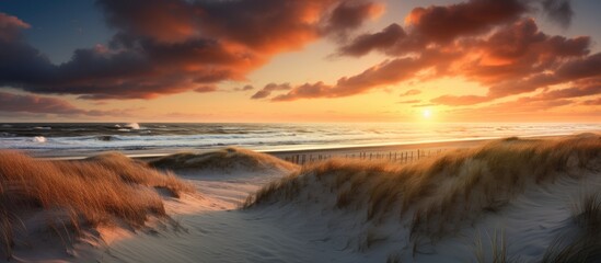The sky is painted with vibrant hues as the sun sets over the beach, casting a warm glow on the sand dunes in the foreground
