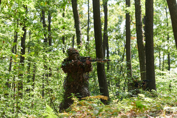 An elite soldier, camouflaged and stealthily navigating through dangerous woodland terrain,...