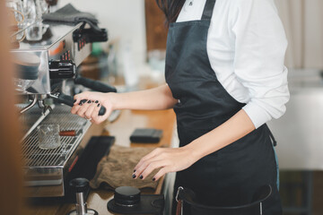 A skilled barista in a black apron expertly operates an espresso machine, focusing on crafting the...