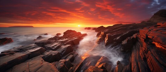 The sunset over a rugged beach with waves crashing against the rocks creates a breathtaking natural landscape with a dramatic sky and tranquil atmosphere