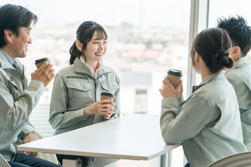 オフィスの休憩所でコーヒーを飲む作業着姿の女性と男性
