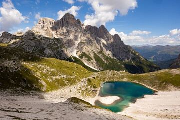 White sandy-rocky slope descends to shore of small lake in Laghi dei piani area with emerald water....