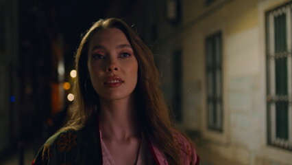 Fototapeta premium Lady walking dark street enjoying night town close up. Woman strolling city
