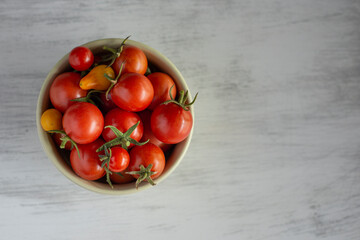 Red small tomatoes in a small green bowl on a light grey surface  