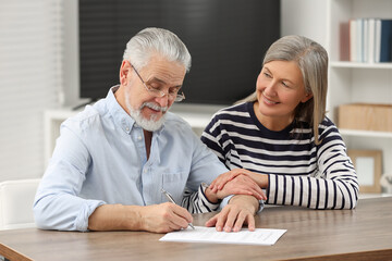 Happy senior couple signing Last Will and Testament indoors