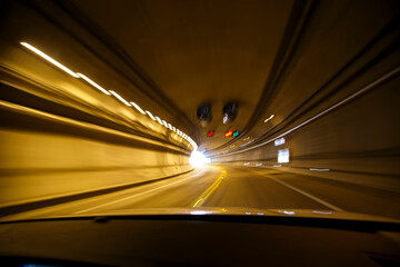 Movimiento rápido. Transitando un túnel curvo en alta velocidad desde un automóvil. Luces ámbar barridas por la rapidez del movimiento. Luz al final del camino. Carretera mexicana. - obrazy, fototapety, plakaty