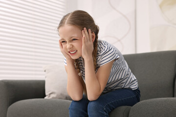 Little girl suffering from headache on sofa indoors