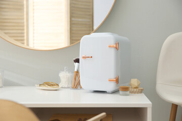 Cosmetics refrigerator and skin care products on white vanity table indoors