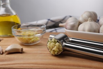 One metal press and garlic on wooden table, closeup