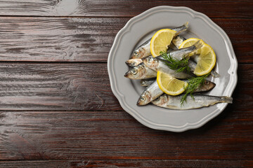 Fresh raw sprats, dill and cut lemon on wooden table, top view. Space for text