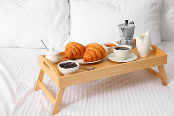 Wooden tray with tasty breakfast on bed