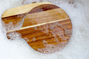 Wooden cutting board in foam of dishwashing liquid.