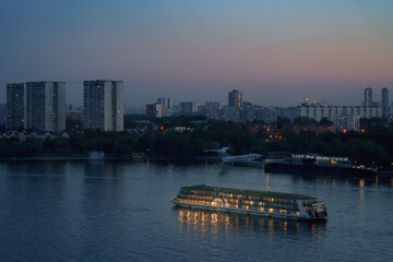 Ship is sailing on river near cityscape at dusk with reflections on the water in the city - 756853814