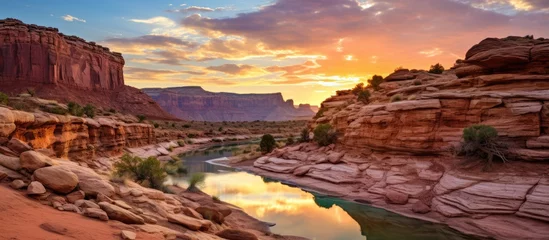 Papier Peint photo Lavable Réflexion A picturesque scene of a river flowing through a canyon at sunset, with the water reflecting the colorful sky and clouds, surrounded by towering mountains and a stunning natural landscape