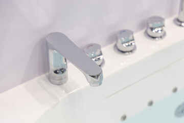 Modern chrome faucet and water taps on a white acrylic bathtub. All parts are made of chromed...