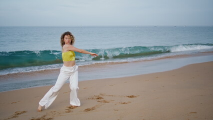 Dancer practicing contemporary choreography at ocean waves. Curly woman dancing