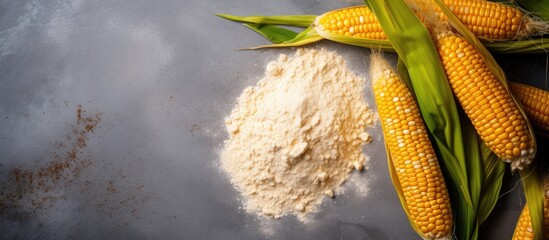 A pile of flour sits next to some freshly picked corn on the cob on a table. The corn is a vegetable from a flowering plant, while the flour is an ingredient made from a terrestrial plant