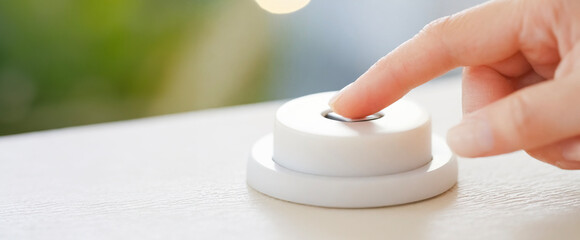 Close-up of a woman's finger pressing a round switch in a brightly lit room - obrazy, fototapety, plakaty