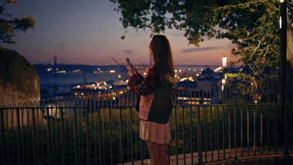 Girl recording night city video on smartphone standing observation deck railings