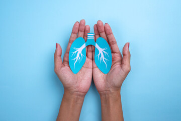 Hands holding healthy lung shape made from paper on blue background.