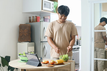 Man making salad while watching online cooking course via tablet in kitchen