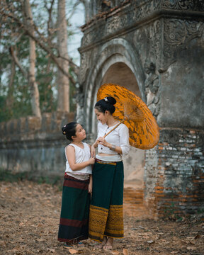 Mother and daughter wearing Thai Traditional dress with an umbrella walking at Wat Mon Jam Sil Temple of ancient Burma according to Thai culture in Lampang Northern Thailand.