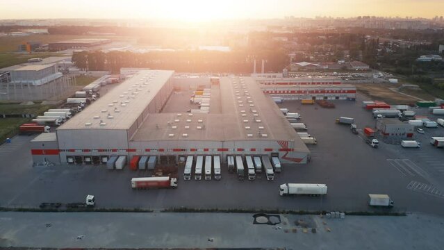 Aerial view of a large logistics park reveals a network of modern warehouses and a bustling loading hub. Semi-trucks with cargo trailers stand docked at ramps, ensuring the efficient movement of goods