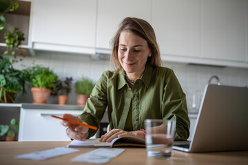 Satisfied female engaged financial receipts at home writing down expenses in diary notebook, paying...