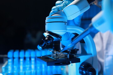A talented scientist sits in his lab while using a microscope to look for microscopic organisms in...