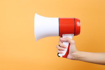 Woman hand holding megaphone over yellow background 
