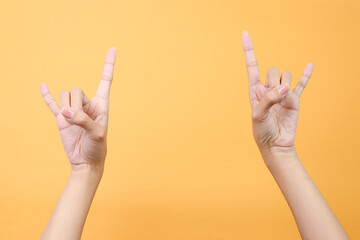 Hands showing rock sign, rock and roll sign hand gesture over yellow background