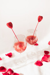 Two wine glasses with fun pink cocktail with heart cocktail stirrers and rose petals for a fun romantic party concept