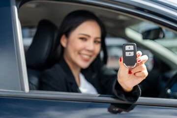 Young beautiful asian business women in suit getting new car showing car key. she very happy and excited in hand holding car key. Smiling female driving vehicle on the road city on a bright day