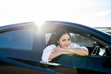 Young beautiful asian business women getting new car. Happy smiling female driving vehicle on the road Sticking her head outta the windshield with sun light. Business woman buying driving new car