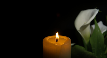 Burning wax candle and white calla lily flowers in darkness