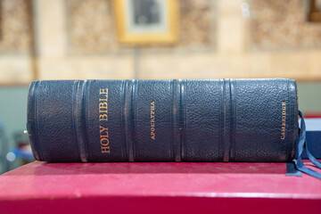 Vintage black leather Holy Bible with Apocrypha inscribed in gold, displayed on a crimson lectern