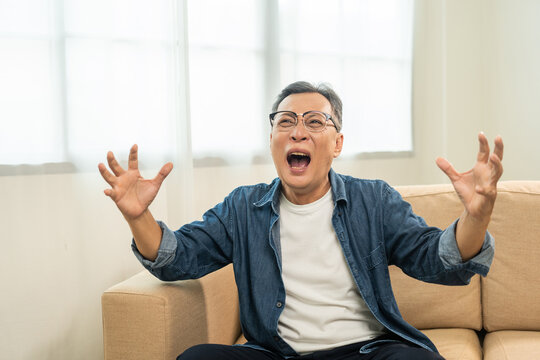 Mad asian mature old man sitting in the house headache crazy angry screaming. Portrait of serious depressed senior asian man. Mature People has problem in life