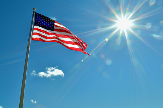 A red, white, and blue American flag is flying in the sky. The sun is shining brightly, casting a warm glow on the flag. Concept of patriotism and pride in the United States