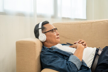 Mature lifestyle relaxing on sofa in the morning. Happy Asian senior old man listening music with...